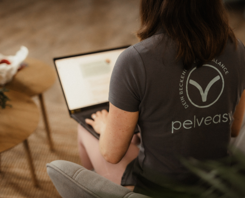Rückansicht Carina Gerlach mit pelveasy Shirt arbeitet am Laptop