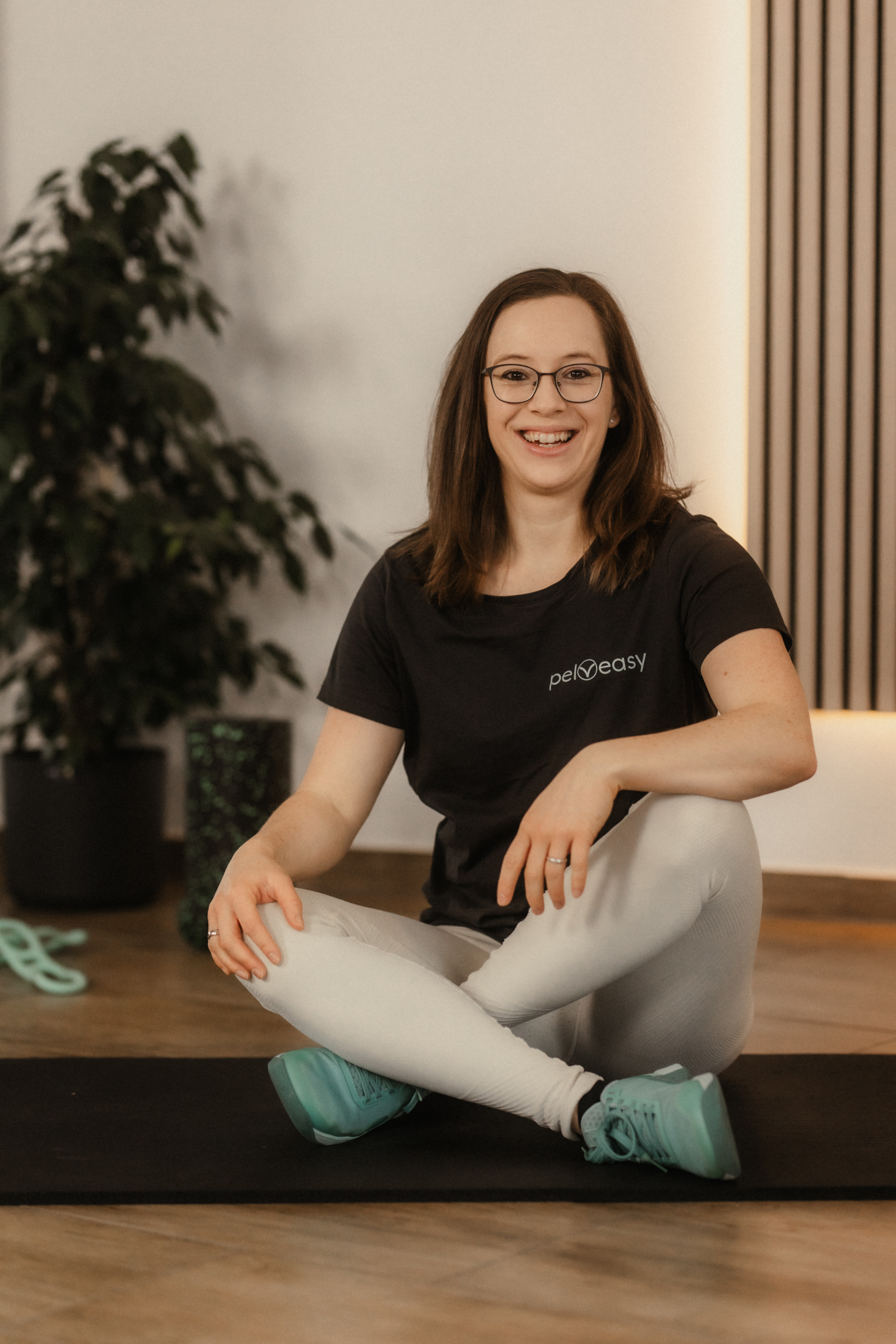 pelveasy Carina Gerlach sitzt im Schneidersitz auf dem Boden und lächelt in die Kamera