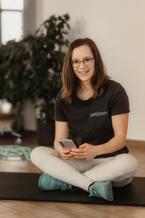 pelveasy Carina Gerlach sitzt mit Smartphone in der Hand auf dem Boden-zeigt Remote Coaching